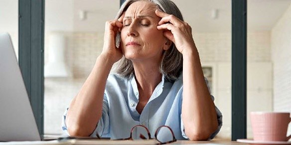 Eine Frau mit grauen Haaren hält sich die Hände vor Stress an die Schläfen