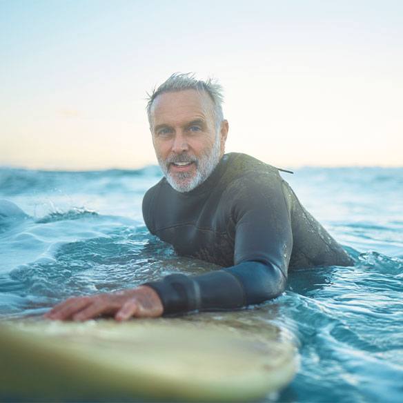 Ein Surfer mittleren Alters mit Surfbrett im Wasser